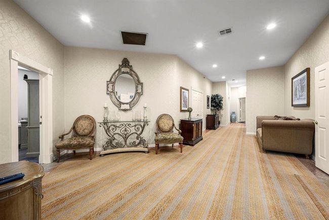 This is a spacious, well-lit hallway with elegant decor, featuring patterned wallpaper, recessed lighting, and plush carpeting. The area is furnished with antique-style chairs, a decorative mirror, and a console table, providing a sophisticated ambiance. Multiple doorways suggest easy access to adjoining rooms. | Image 22