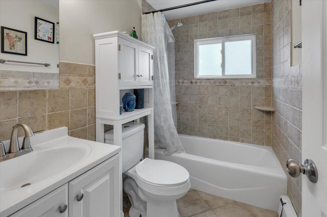 Bathroom with tile patterned flooring, toilet, baseboard heating, shower / bath combination with curtain, and tile walls | Image 10