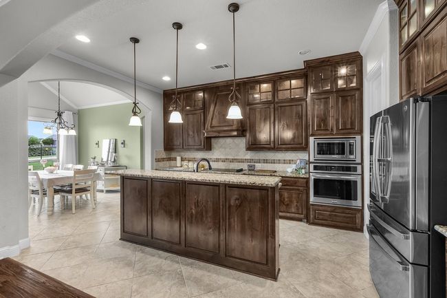 Kitchen with stainless steel appliances, premium range hood, decorative backsplash, crown molding, and a chandelier | Image 22
