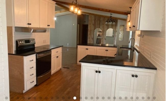 Kitchen with a peninsula, stainless steel electric range oven, dark countertops, under cabinet range hood, and a sink | Image 20