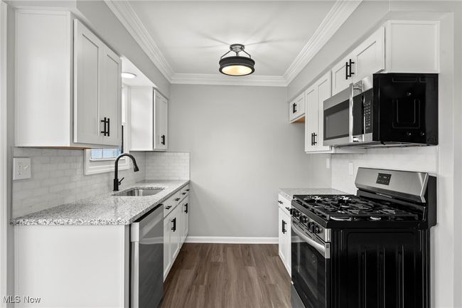 Kitchen with dark wood finished floors, light stone countertops, appliances with stainless steel finishes, a sink, and crown molding | Image 15