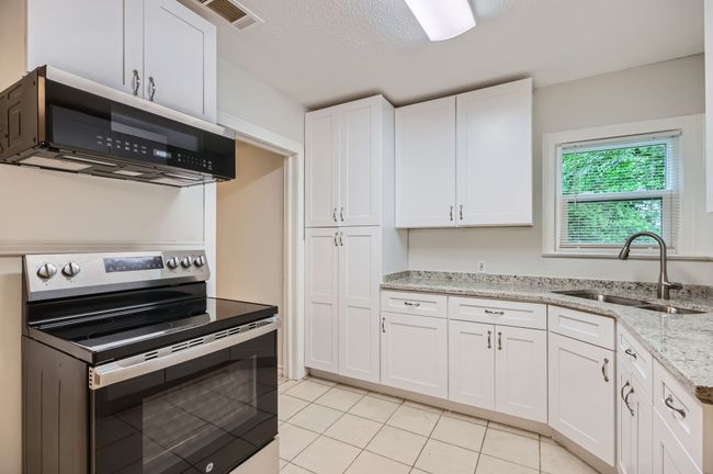 Kitchen with light tile patterned flooring, a sink, white cabinets, and stainless steel appliances | Image 13