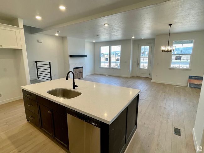 Kitchen with dishwasher, a fireplace, light wood finished floors, light countertops, and open floor plan | Image 4