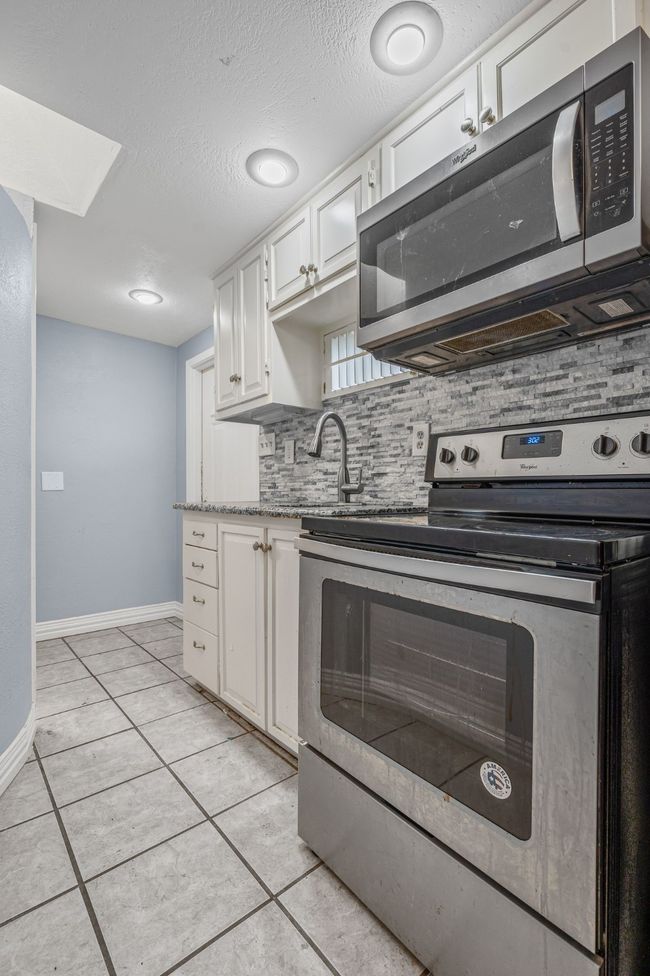 Kitchen with appliances with stainless steel finishes, decorative backsplash, white cabinets, light tile patterned flooring, and a textured ceiling | Image 23