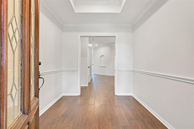 Step through a solid mahogany and leaded glass door into a bright entry hall showcasing rich engineered wood floors, crisp white crown molding, chair rail detailing, and a striking trayed ceiling that adds dimension and elegance. | Image 5
