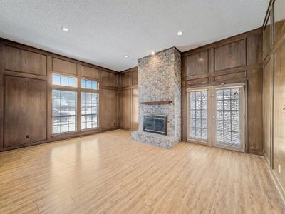 Unfurnished living room with light hardwood / wood-style flooring, wood walls, plenty of natural light, and a brick fireplace | Image 3