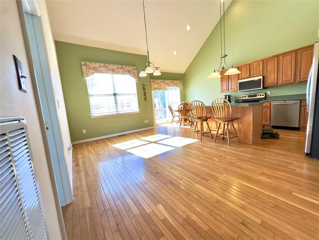 Kitchen with stainless steel appliances, dark countertops, light wood-style floors, high vaulted ceiling, and a kitchen bar | Image 4