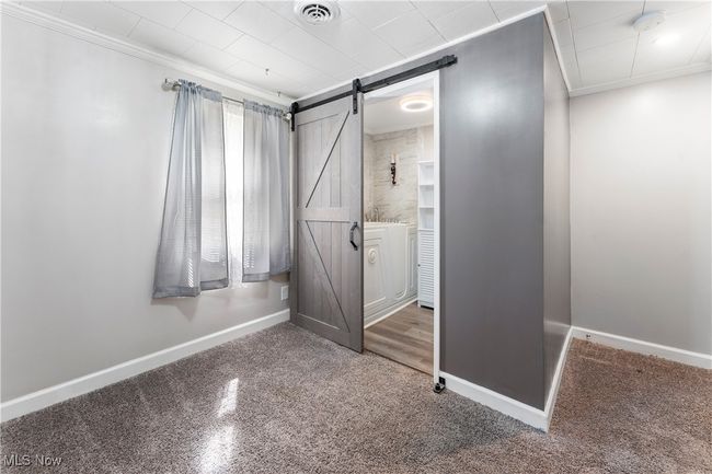 Unfurnished bedroom featuring crown molding, visible vents, a barn door, and baseboards | Image 27