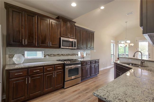 Kitchen with stainless steel appliances, light wood finished floors, a chandelier, tasteful backsplash, and light stone counters | Image 12