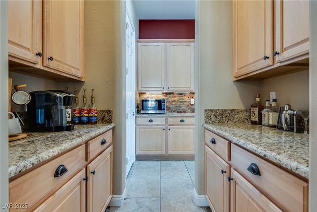 Kitchen with light tile patterned flooring, light stone countertops, stainless steel microwave, tasteful backsplash, and light brown cabinetry | Image 20