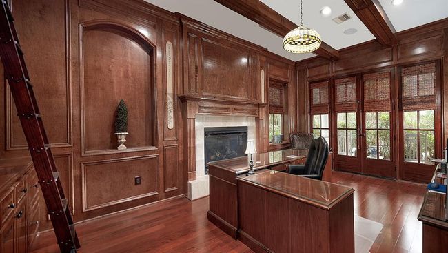 The wood paneled study features a cozy fireplace, library ladder and wood beam ceiling | Image 9