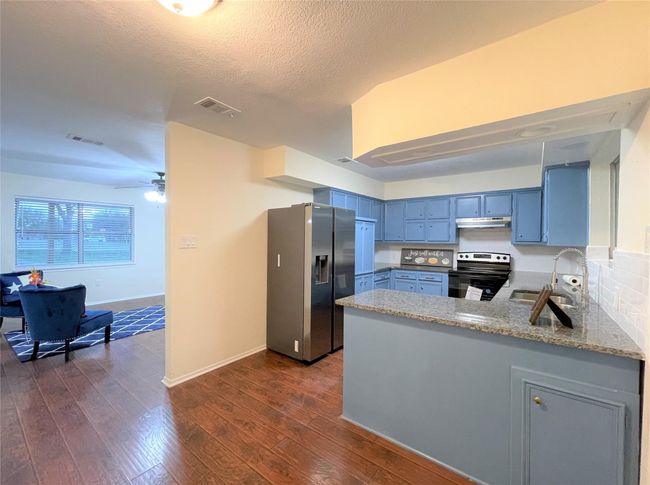 Kitchen featuring electric stove, stainless steel fridge with ice dispenser, under cabinet range hood, blue cabinetry, and a peninsula | Image 9