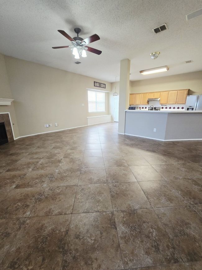 Unfurnished living room with ceiling fan, a textured ceiling, a tiled fireplace, and baseboards | Image 11