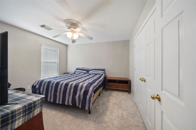 Cozy bedroom with neutral walls and carpet, featuring a ceiling fan and a window for natural light. The room includes a closet with double doors, offering ample storage space. | Image 27