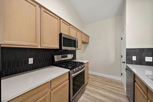 Kitchen featuring appliances with stainless steel finishes, light brown cabinetry, vaulted ceiling, decorative backsplash, and light wood finished floors | Image 12