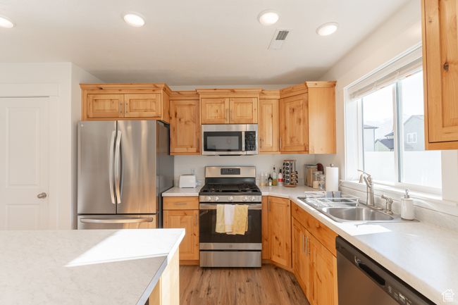 Kitchen with light wood-style flooring, visible vents, appliances with stainless steel finishes, light countertops, and a sink | Image 7
