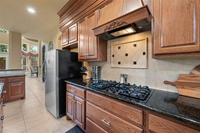Kitchen with black gas cooktop, custom range hood, backsplash, freestanding refrigerator, and light tile patterned floors | Image 16