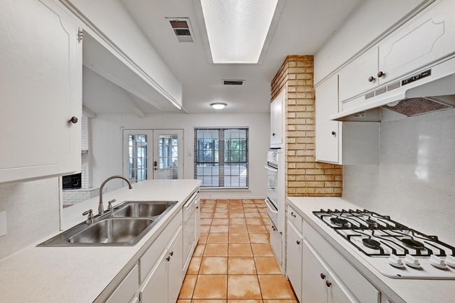 Kitchen with visible vents, a sink, white appliances, under cabinet range hood, and backsplash | Image 15