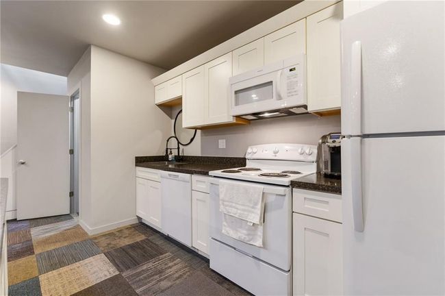 Kitchen with sink, white appliances, dark tile floors, and white cabinetry | Image 19