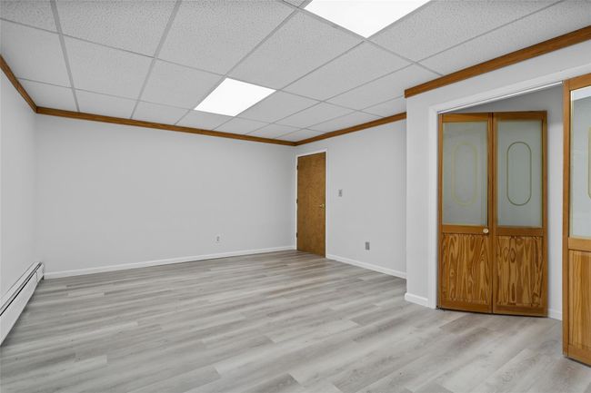 Empty room with crown molding, a baseboard radiator, light wood finished floors, and a drop ceiling | Image 27