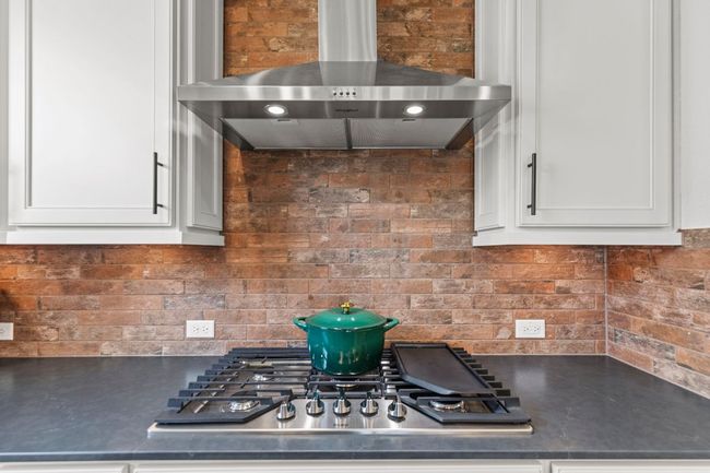 Kitchen with stainless steel gas stovetop, range hood, dark countertops, decorative backsplash, and white cabinetry | Image 12