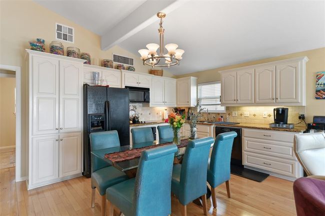 This kitchen features high ceilings and ample natural light. It has granite countertops, white shaker cabinetry, black appliances. The space is open and inviting, ideal for gatherings. | Image 16