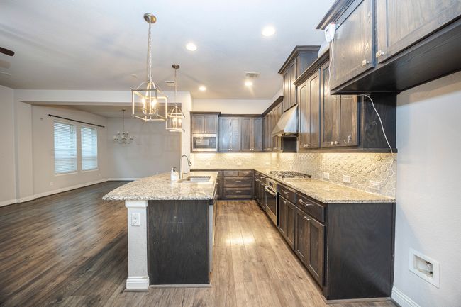 Kitchen featuring stainless steel appliances, a chandelier, dark brown cabinetry, range hood, and light stone countertops | Image 19