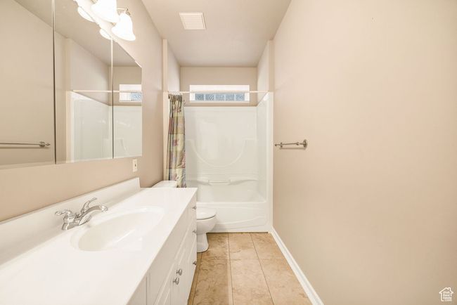 Full bathroom with vanity, toilet, tile patterned floors, shower / tub combo with curtain, and baseboards | Image 32