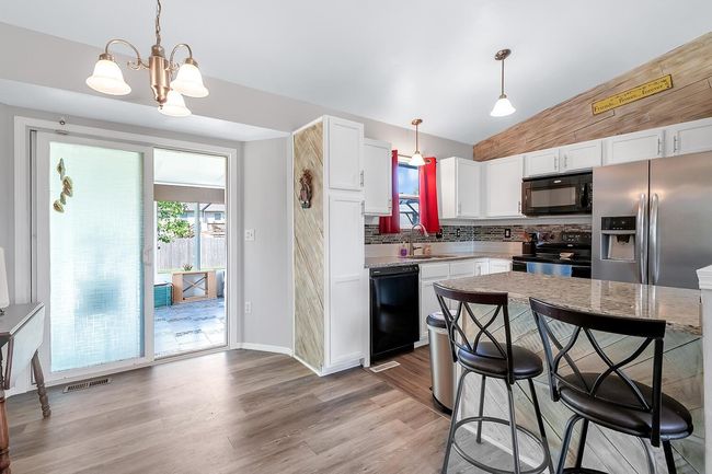Kitchen featuring black appliances, white cabinetry, light wood-type flooring, backsplash, and a breakfast bar area | Image 11