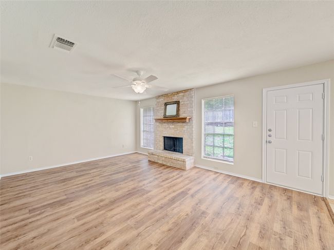 Unfurnished living room featuring light wood finished floors, a ceiling fan, baseboards, a brick fireplace, and a textured ceiling | Image 4