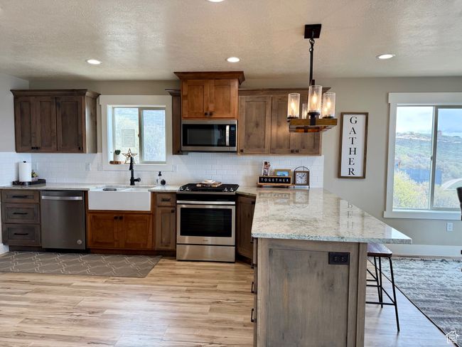 Kitchen featuring a breakfast bar area, appliances with stainless steel finishes, a sink, a peninsula, and light wood-style floors | Image 21