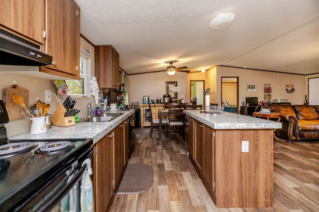 Kitchen featuring light countertops, black electric range, under cabinet range hood, brown cabinetry, and ceiling fan | Image 8