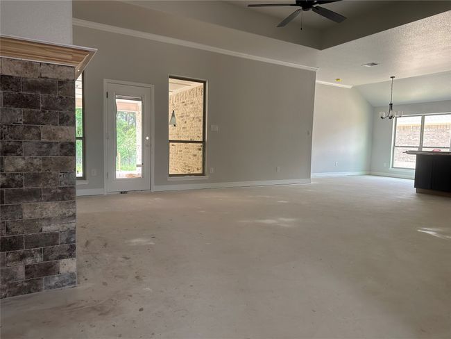 Unfurnished living room featuring ceiling fan with notable chandelier, visible vents, baseboards, unfinished concrete floors, and ornamental molding | Image 6