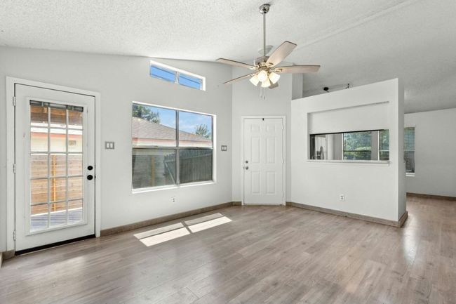 living room with a textured ceiling, light wood-style floors, high vaulted ceiling, and a ceiling fan | Image 10