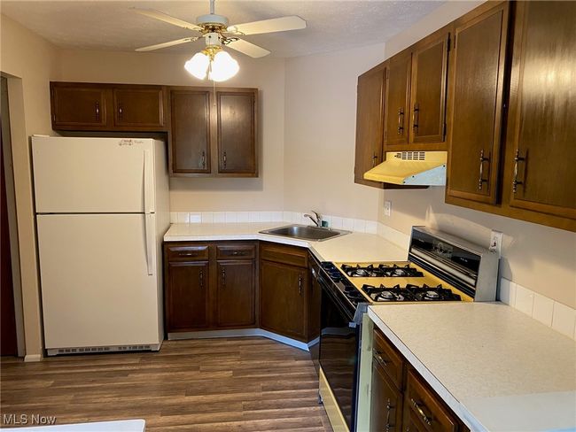 Kitchen with a sink, dark wood-style flooring, freestanding refrigerator, range with gas stovetop, and under cabinet range hood | Image 4