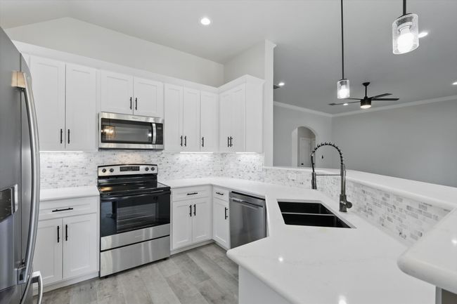Kitchen with stainless steel appliances, a sink, light wood-type flooring, decorative backsplash, and crown molding | Image 11