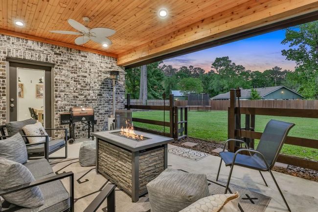 This cozy outdoor patio features a wooden ceiling with recessed lighting and a ceiling fan, a modern fire pit with comfortable seating, and a view of a spacious backyard. Ideal for relaxation and entertaining. | Image 6