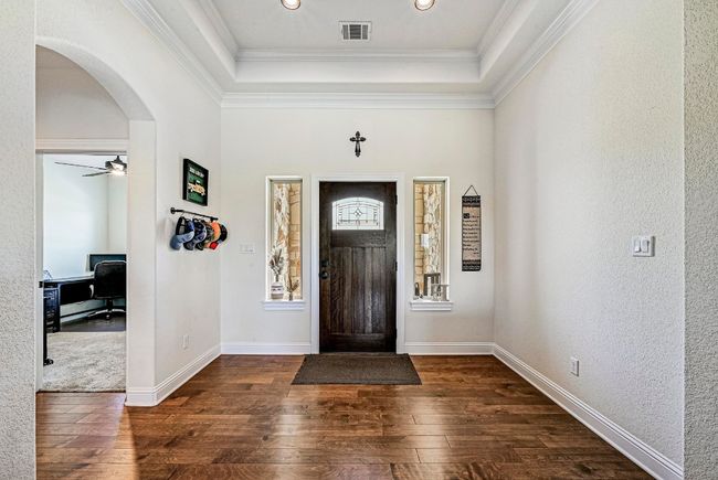 Entryway featuring dark wood-style flooring, arched walkways, a raised ceiling, a textured wall, and crown molding | Image 4