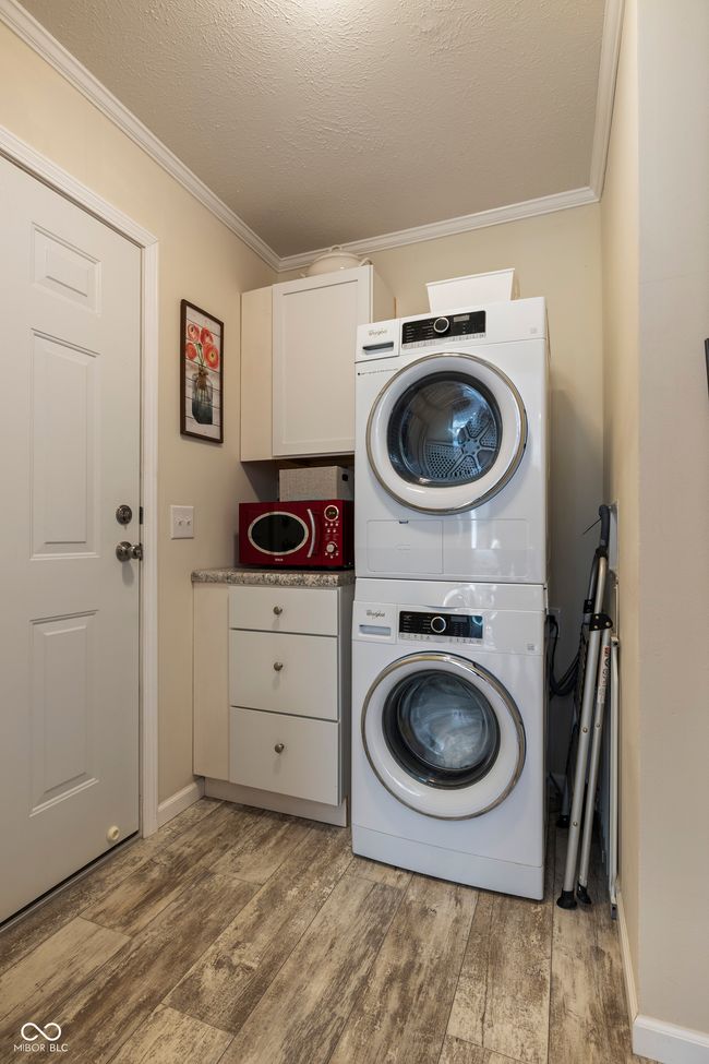washroom with estacked washer and dryer, ornamental molding, cabinet space, and wood finished floors | Image 32