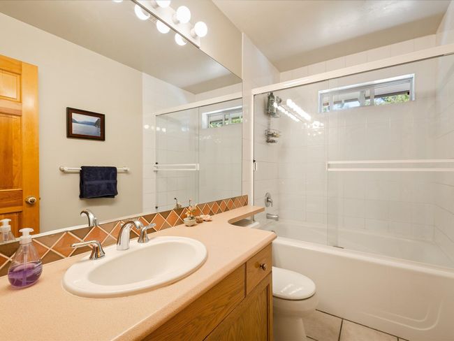 Full bath featuring vanity, enclosed tub / shower combo, tile patterned flooring, toilet, and decorative backsplash | Image 11