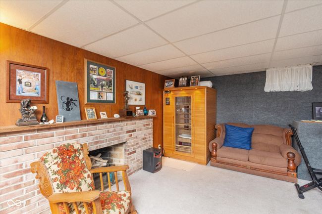 living area featuring a paneled ceiling, carpet flooring, wooden walls, and a brick fireplace | Image 21