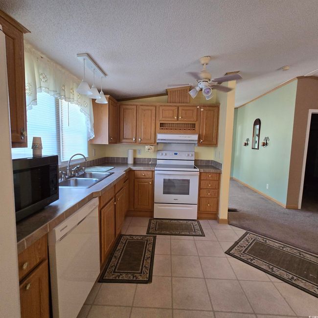 Kitchen with light tile patterned floors, vaulted ceiling, white appliances, a textured ceiling, and a ceiling fan | Image 17