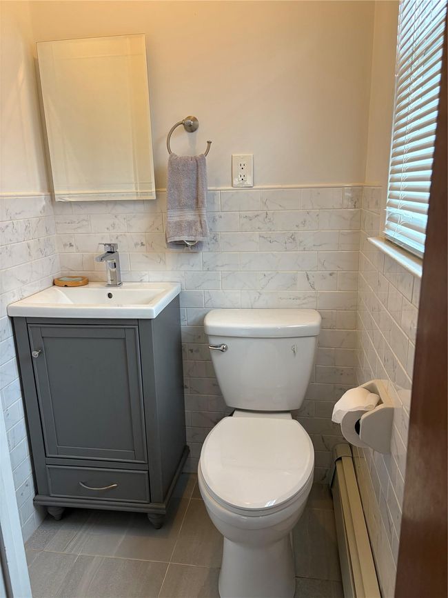 Half bath featuring toilet, vanity, baseboard heating, wainscoting, and tile patterned flooring | Image 9
