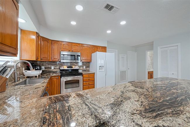 Modern kitchen featuring granite countertops, stainless steel appliances, and warm wooden cabinetry. Bright lighting and ample space enhance functionality. | Image 12