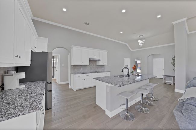 Kitchen with arched walkways, a sink, ornamental molding, under cabinet range hood, and white cabinetry | Image 12