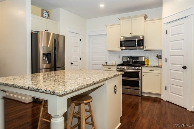 Kitchen featuring decorative backsplash, light stone countertops, stainless steel appliances, dark wood-type flooring, and a breakfast bar area | Image 12