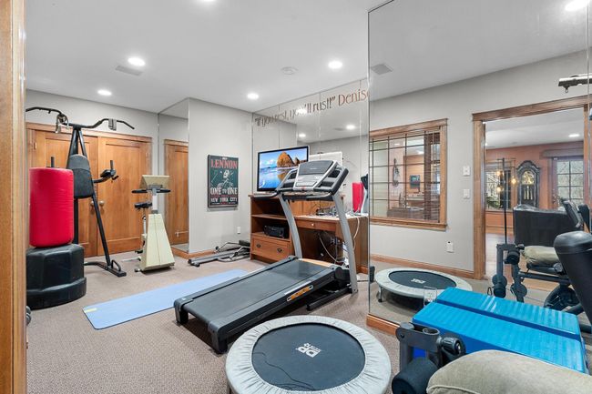 Lower-level exercise room with space for several machines and weights. Mirrored walls and French, windowed doors to lower-level hallway. Ceiling speakers connect to media cabinet. Exercise equipment included. | Image 47