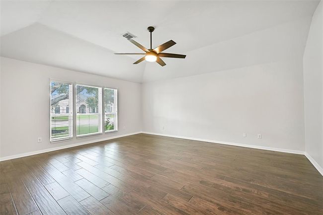 Secluded at the front of the home, this expansive primary suite showcases engineered wood floors, a soaring 10' gambrel ceiling with a modern lighted fan, and a wall of front-facing windows for abundant natural light. | Image 16