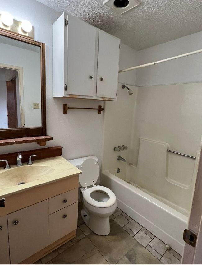 Bathroom featuring a textured ceiling, vanity, shower / washtub combination, toilet, and tile patterned flooring | Image 9