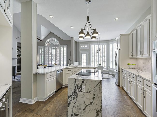 Kitchen featuring stainless steel appliances, a chandelier, a kitchen island, dark wood-style floors, and white cabinets | Image 14